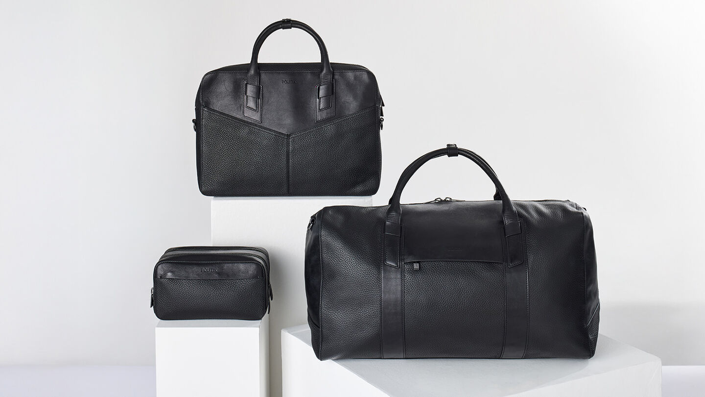 Black leather weekender bag, briefcase, and toiletry bag styled on white pedestals — premium men’s gift ideas over $250