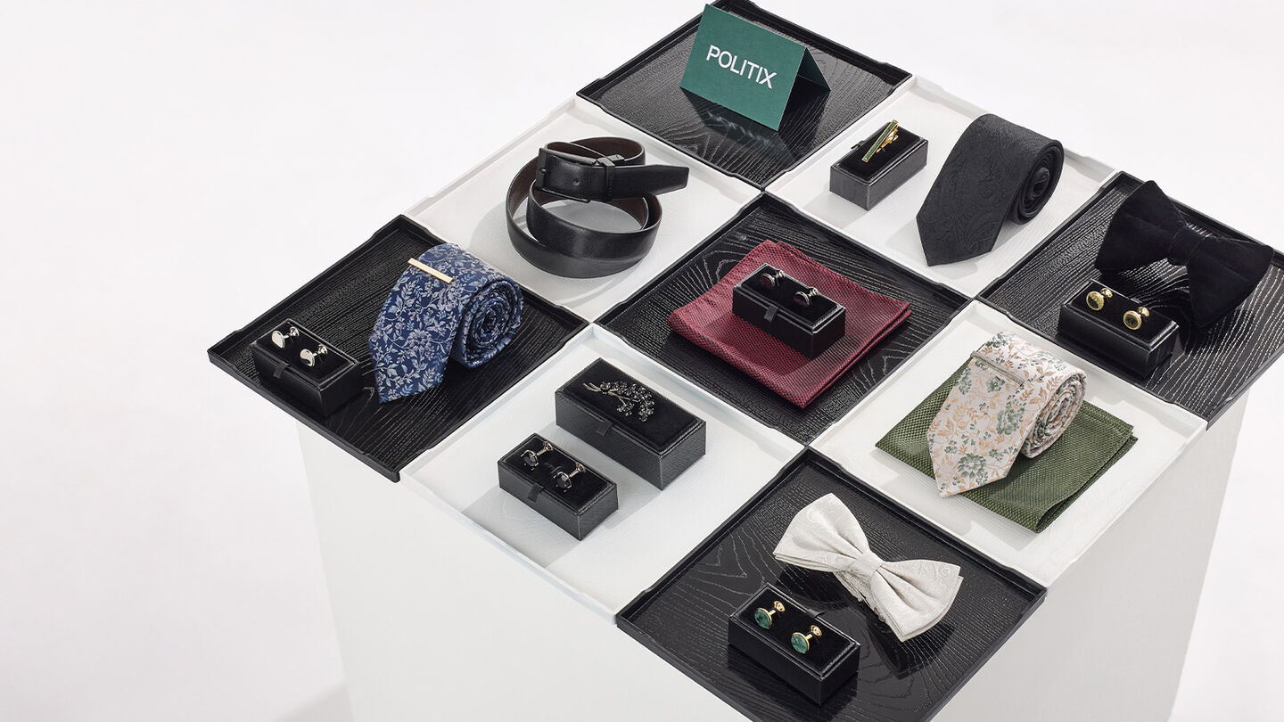 Men’s accessories gift set under $50 featuring cufflinks, bow ties, patterned ties, tie bars and belts arranged in a grid display from POLITIX.