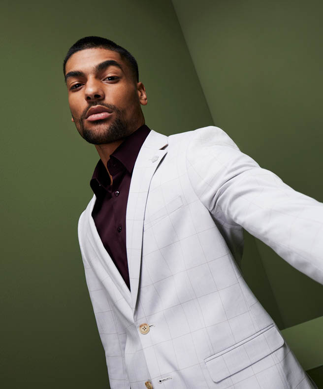 Model with his arm raised in front of dark green wall wearing POLITIX stone suit jacket and burgundy button up shirt 