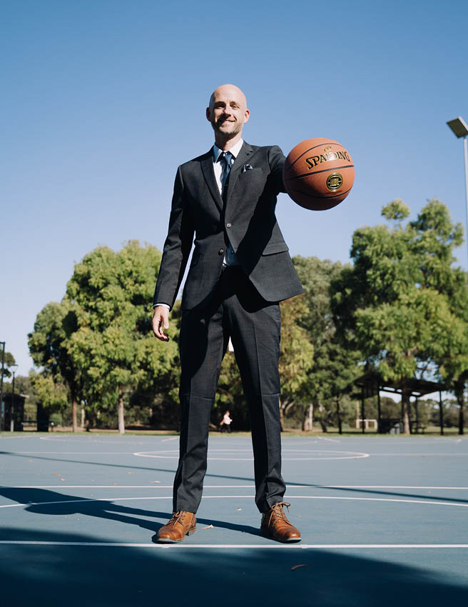 Jarrod Walsh standing on blue basketball court wearing dark grey POLITIX suit holding basketball