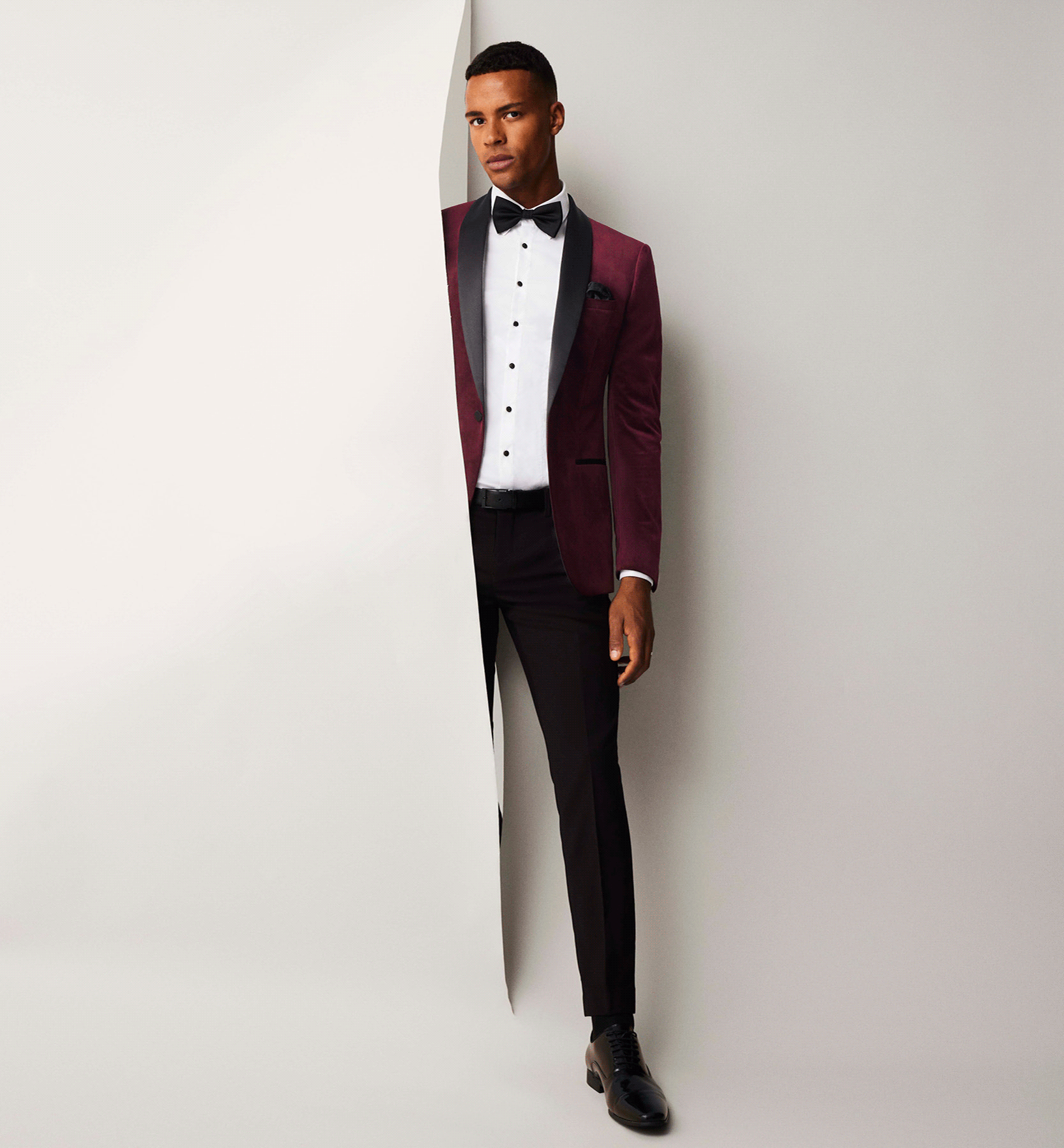 Make An Entrance Model wearing burgundy black tie suit stepping out of a white wall