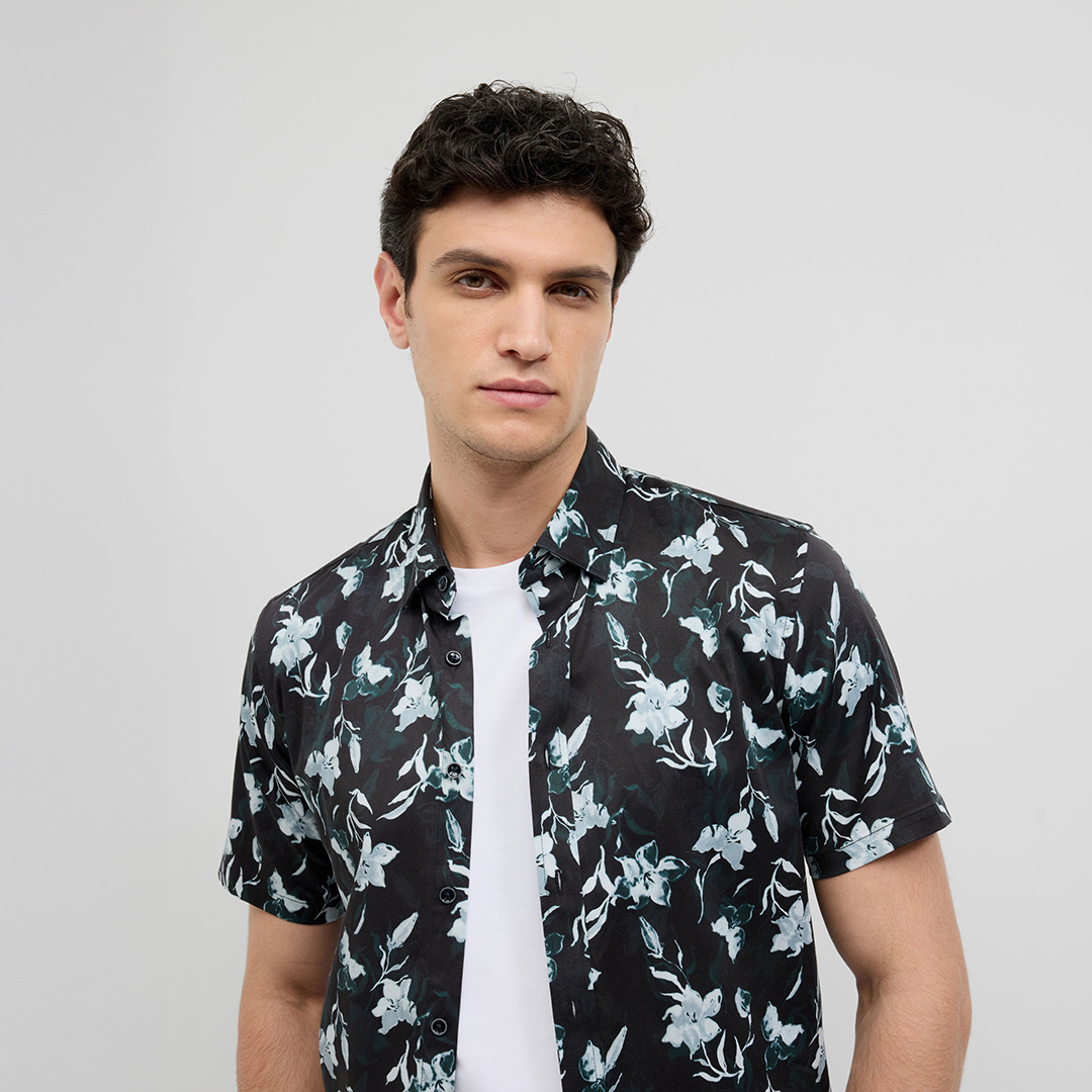 Man wearing a black short sleeve shadow floral print shirt with teal accents over a white tee.