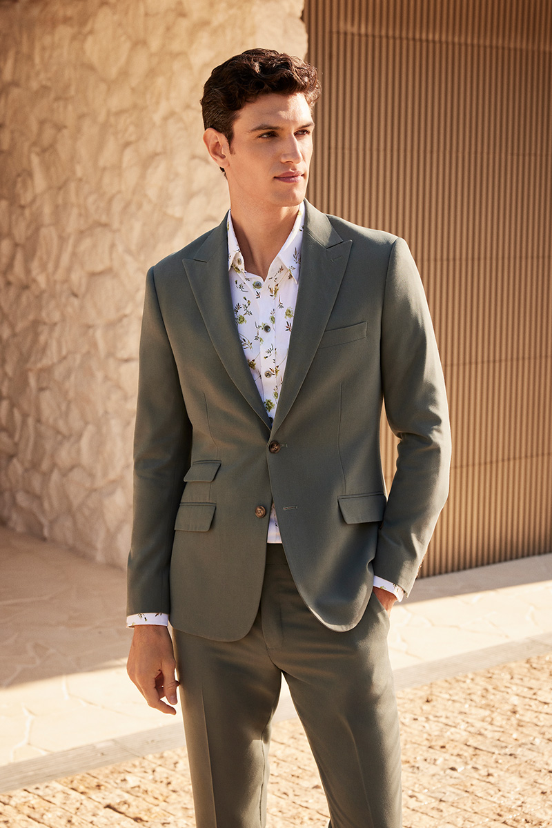 Model wearing POLITIX Spring Summer 2025 sage slim-fit stretch suit with floral shirt – modern tailored menswear for weddings, work, and events.