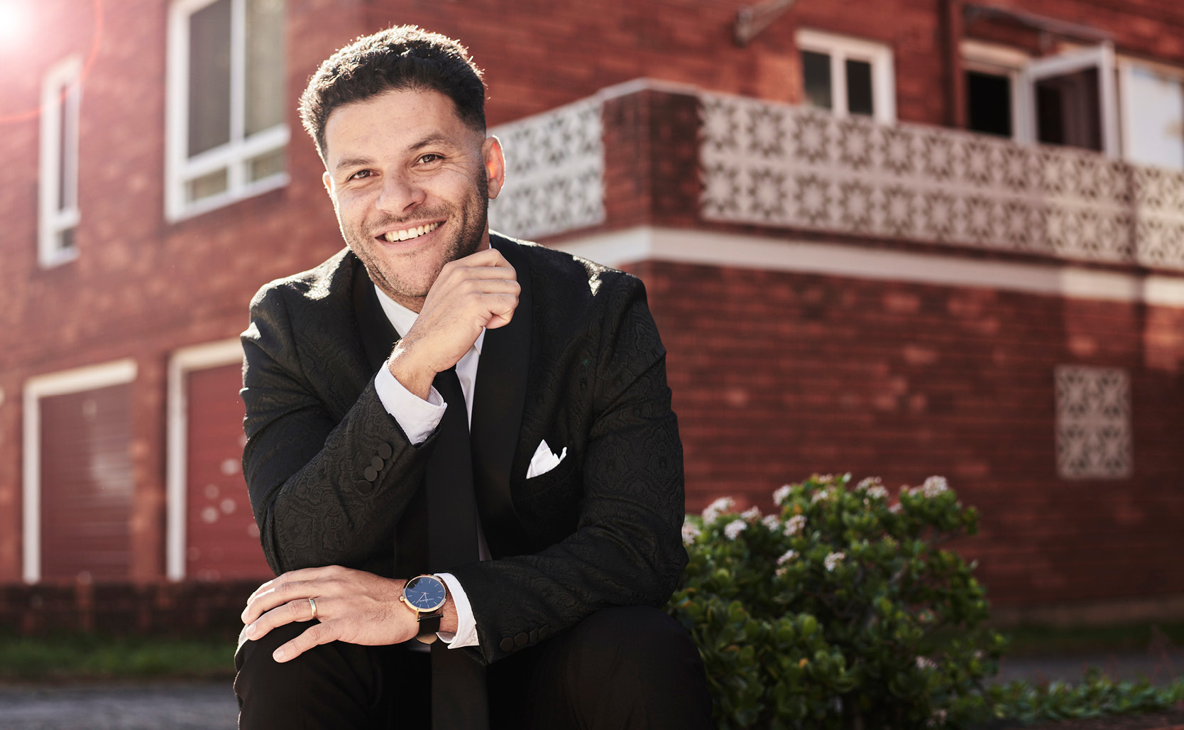 Kid Mac featuring POLITIX Kid Mac smiling in front of brick building wearing POLITIX Black suit