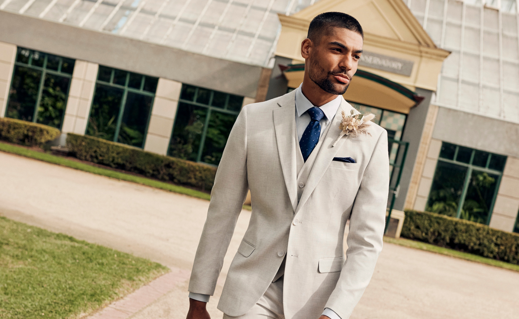 POLITIX Stone Suit Model walking towards camera in park setting wearing POLITIX stone suit, white button up shirt and blue tie & pocket square