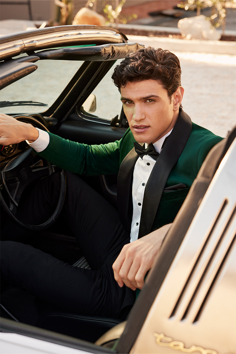 Model in POLITIX Spring Summer 2025 emerald velvet tuxedo with black satin lapels and bow tie, seated in a vintage convertible – luxury men’s black tie eventwear.