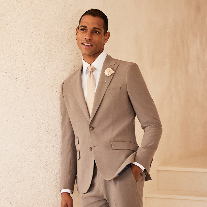 Model in POLITIX Spring Summer 2025 mushroom suit styled with cream tie and crisp white shirt – neutral tailoring trend for men’s weddings and milestone celebrations